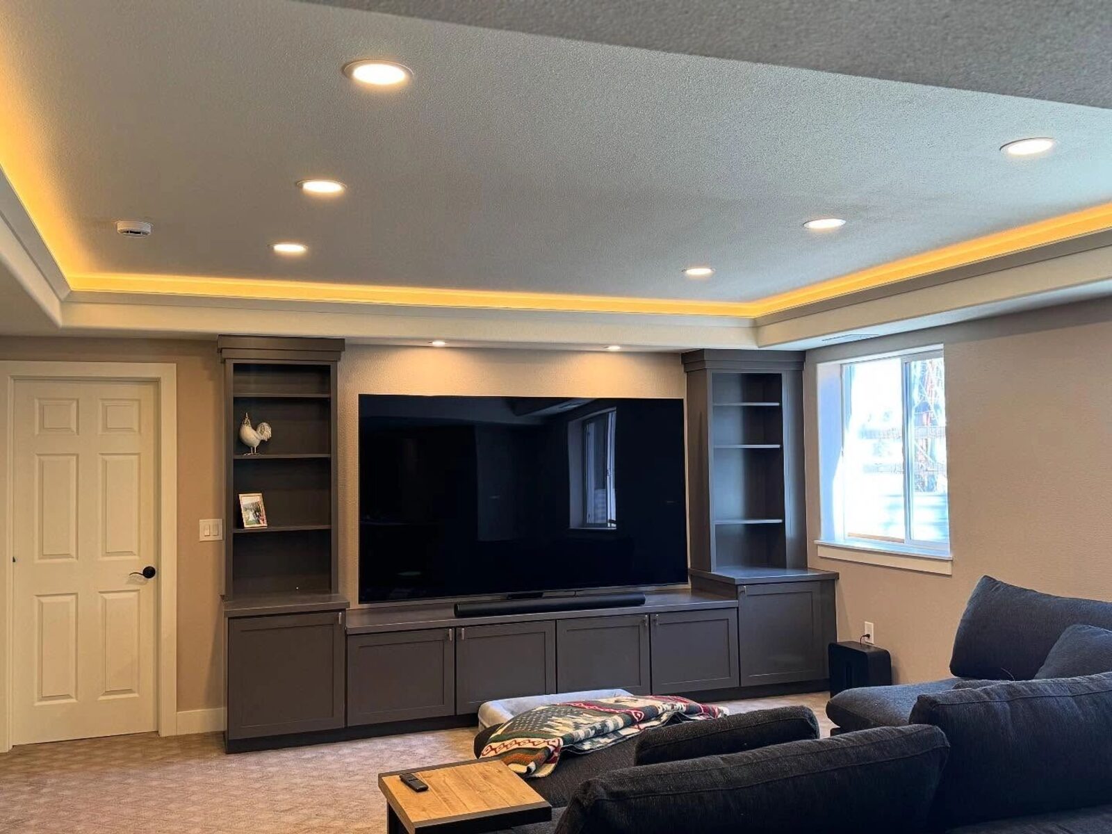 Finished basement media room with cove lighting around a tray ceiling and a built-in media wall.